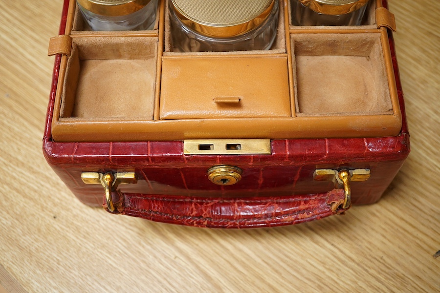 A red stained crocodile skin two layer vanity case, fitted with brass topped bottles and pots, case 22cm wide x 13.5cm high. Condition - handle has pulled away one side and needs re stitching